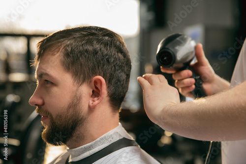 Delighted. Close up of client of master barber, stylist during getting care and new look of hairstyle. Professional occupation, male beauty and self-care concept. Soft colors and focus, vintage.