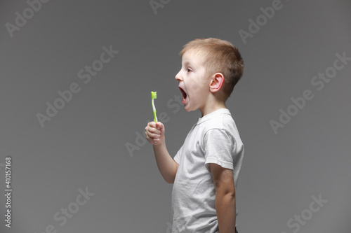 Happy child kid boy with electric toothbrush on gray background. Health care, dental hygiene. Mockup, copy space photo