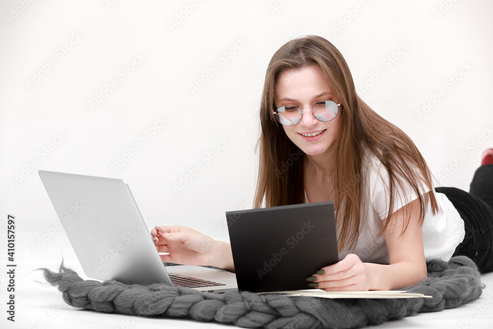 Naklejka premium A smiling young girl in glasses sits with a laptop. Education, remote work and blogging. Isolated on a white background.