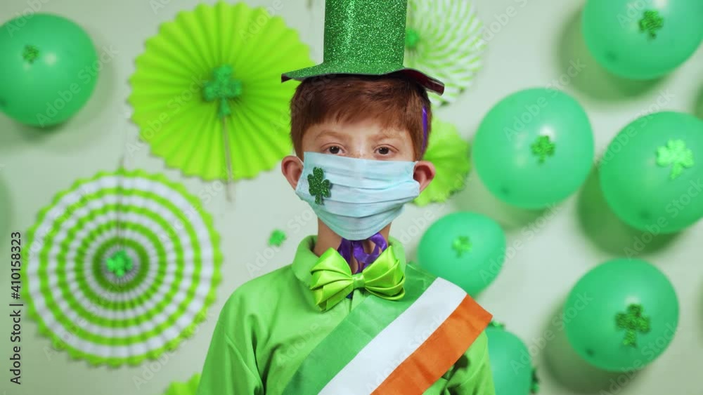 Upward pan shot of kid wearing medical face mask with shamrock sticker as coronavirus covid-19 safety measures during saint Patricks day festival celebration Upward pan shot of kid wearing medical face mask with shamrock sticker as coronavirus covid-19 safety measures during saint Patricks day festival celebration