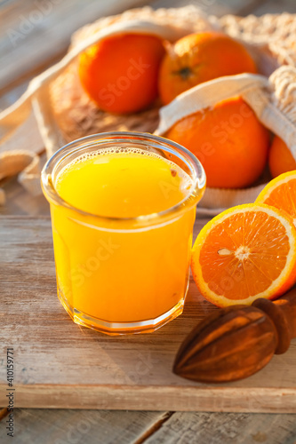 Glass of freshly sqeezed orange juice on a wooden table. Natural source of vitamins, healthy beverage for ideal breakfast. Bright sunny summer day. Close up, copy space for text.