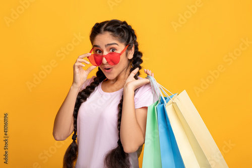 Indian woman in glasses holding colorful shopping bags at studio