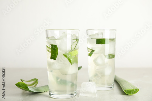 Fresh aloe drink in glasses and leaves on light table