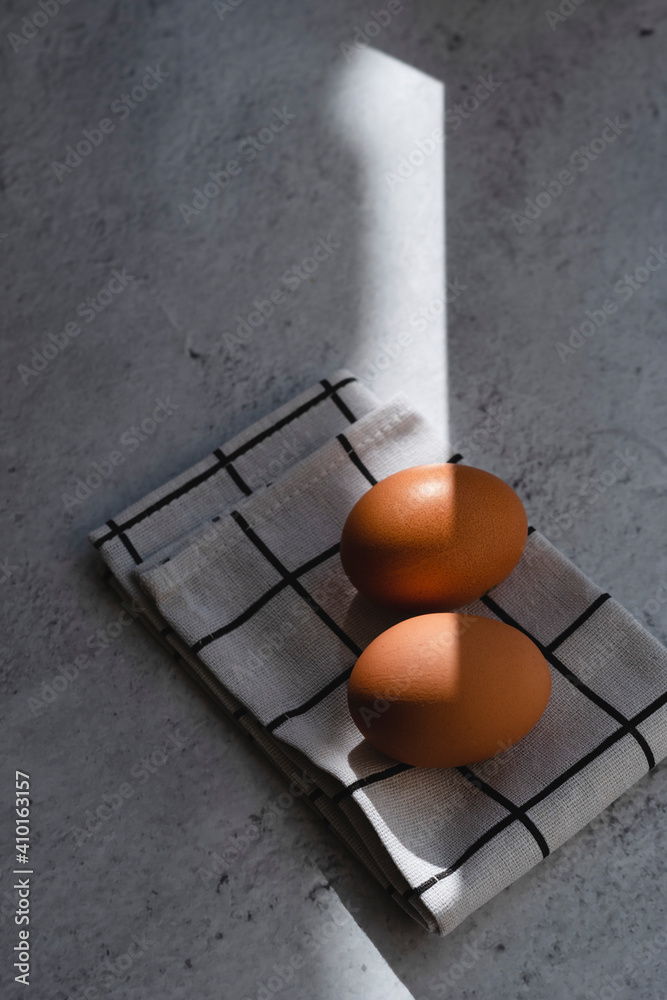 Chicken eggs lie on a white checkered napkin on a concrete background