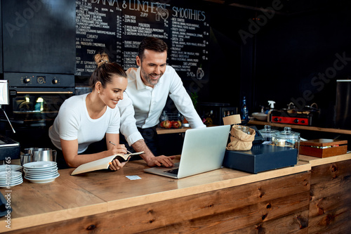 Happy small business owners working with laptop at cafe photo
