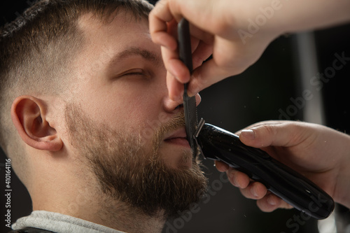 Close up of client of master barber, stylist during getting care and new look of mustache and beard. Professional occupation, male beauty and self-care concept. Soft colors and focus, vintage.