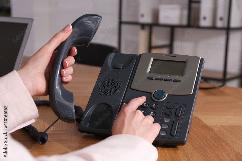 Woman using desktop telephone at wooden table in office, closeup. Hotline service Woman using desktop telephone at wooden table in office, closeup. Hotline service