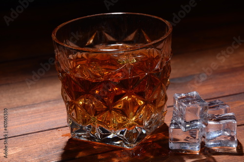 Glass of whisky or whiskey or bourbon on ice  on wood bar