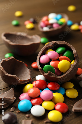 Broken chocolate eggs and colorful candies on wooden table, closeup