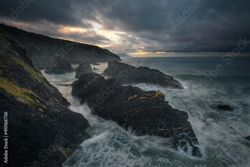 Stormy seascape sunset scene with black rocks