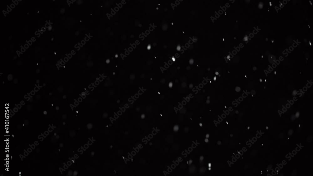 Winter falling snow on black background. Small snow snowflakes falling in the dark. Backlit white snowflakes at night