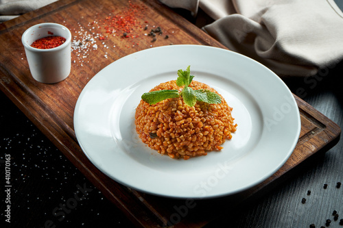 Appetizing and healthy side dish - bulgur in red sauce with Turkish spices in a white plate on a dark background photo