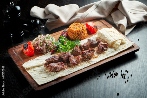 Appetizing beef kebab with grilled vegetables, bulgur and pickled onions on a wooden board