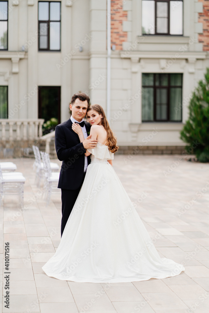 beautiful newlyweds stand against the background of a light building. 