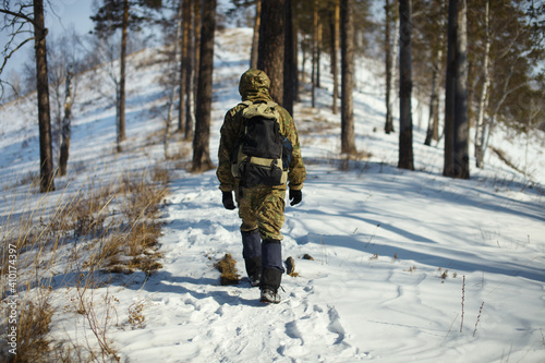 Extreme traveller with a backpack walking in a mountainous area overgrown with coniferous forest, rear view, close-up.