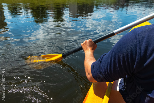Close up shot of person canoeing in the river on a sunny day. Hands holding a paddle and rowing in flowing water