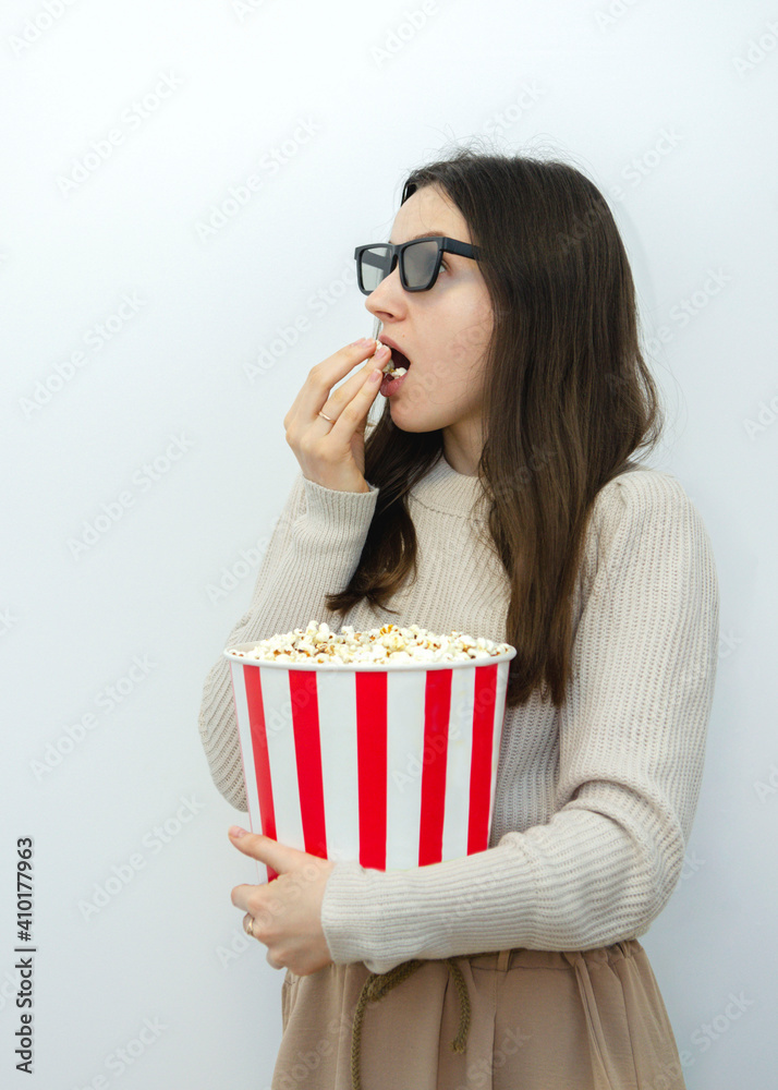 Young beautiful woman eating popcorn from a red and white striped basket and watching tv Young beautiful woman eating popcorn from a red and white striped basket and watching tv