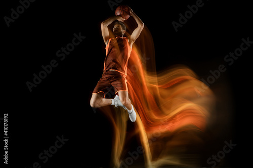 Slam dunk. Young arabian muscular basketball player in action, motion isolated on black background in mixed light. Concept of sport, movement, energy and dynamic, healthy lifestyle. Training