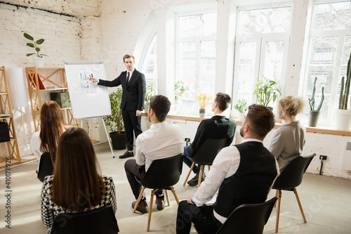 Graphs. Male speaker giving presentation in hall at university workshop. Audience or conference hall. Rear view of unrecognized participants. Scientific, business conference event, training. Education