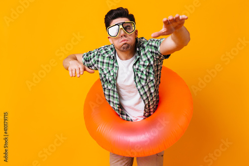 Man in green shirt, diving mask and inflatable circle represents swimming on orange background