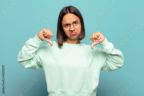 young hispanic woman looking sad, disappointed or angry, showing thumbs down in disagreement, feeling frustrated photo