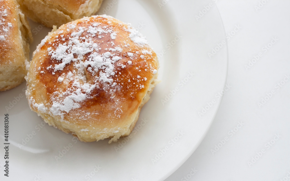 Delicious buns with powdered sugar on a white plate on a white background