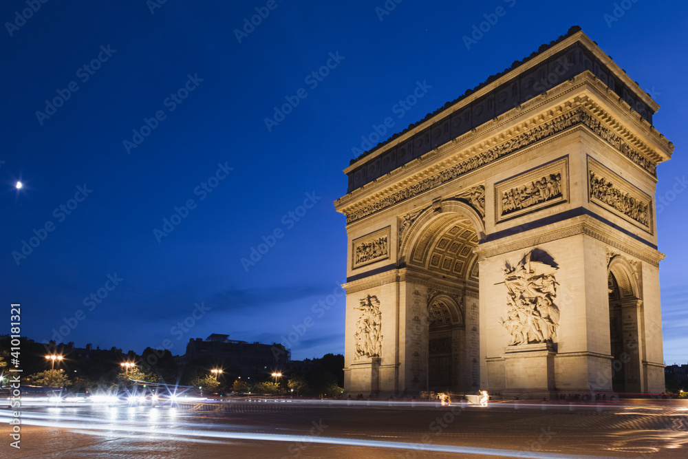 Light trails left behind from buzzing motor traffic around the landmark Arc de Triomphe at night in Paris, France