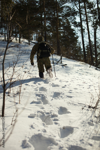 Traveller with a backpack overcomes deep snow drifts during a walk through the winter forest in sunny frosty weather, close-up, rear view.