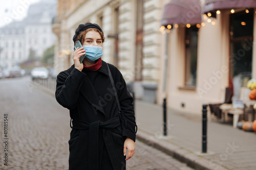 Stylish woman in mask having mobile conversation on street