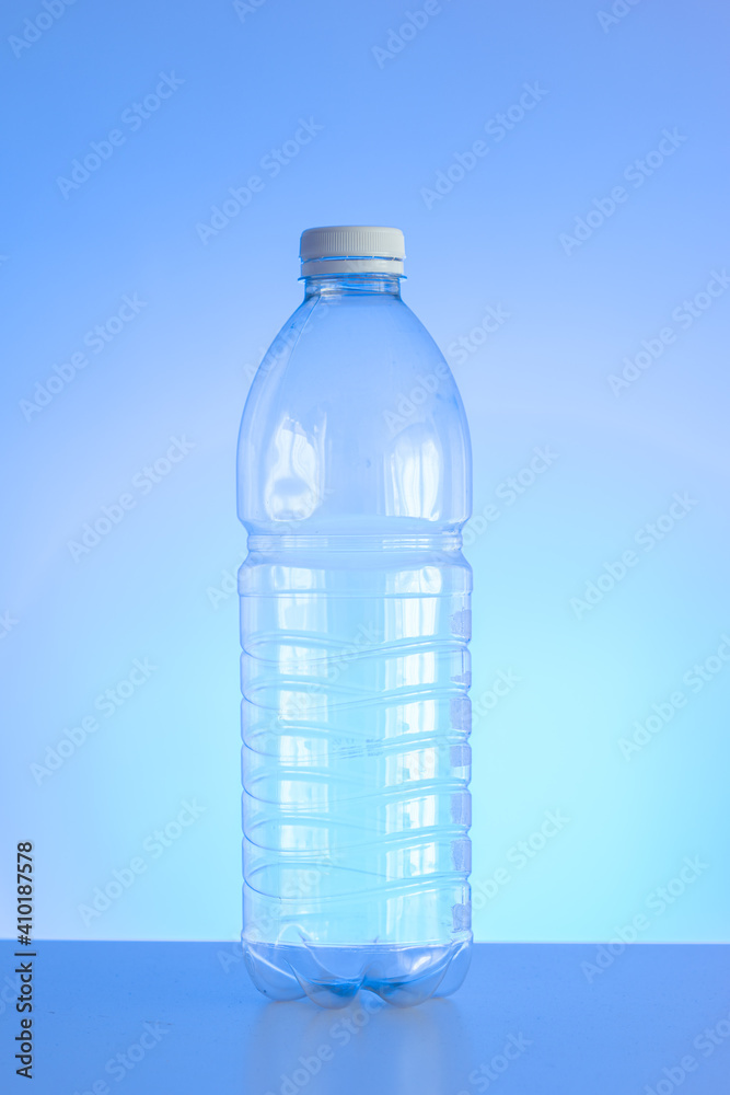 Clear empty plastic bottle with red lid isolated on light blue background vertical shot