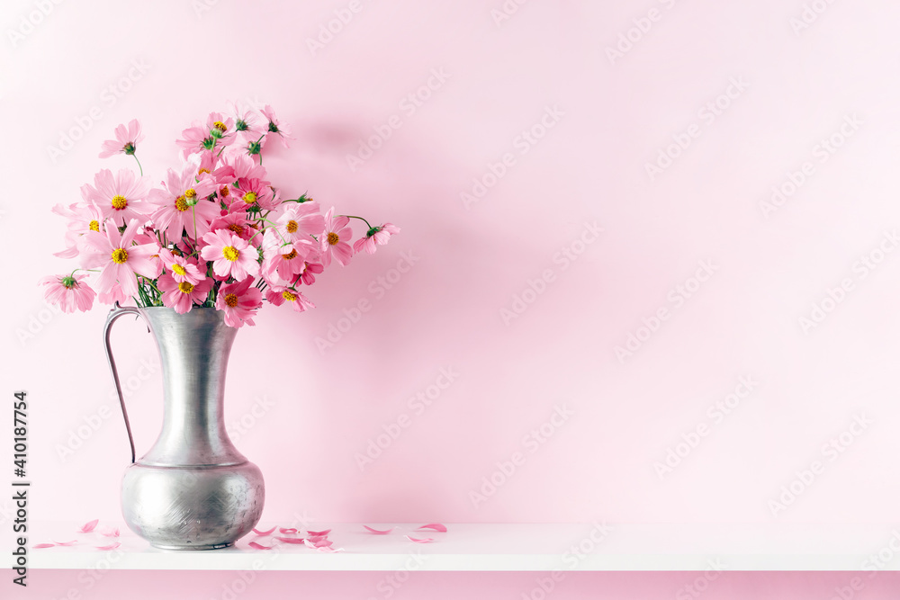 Fresh summer bouquet of pink cosmos flowers in vase on white wood shelf on pink wall background. Floral home decor.