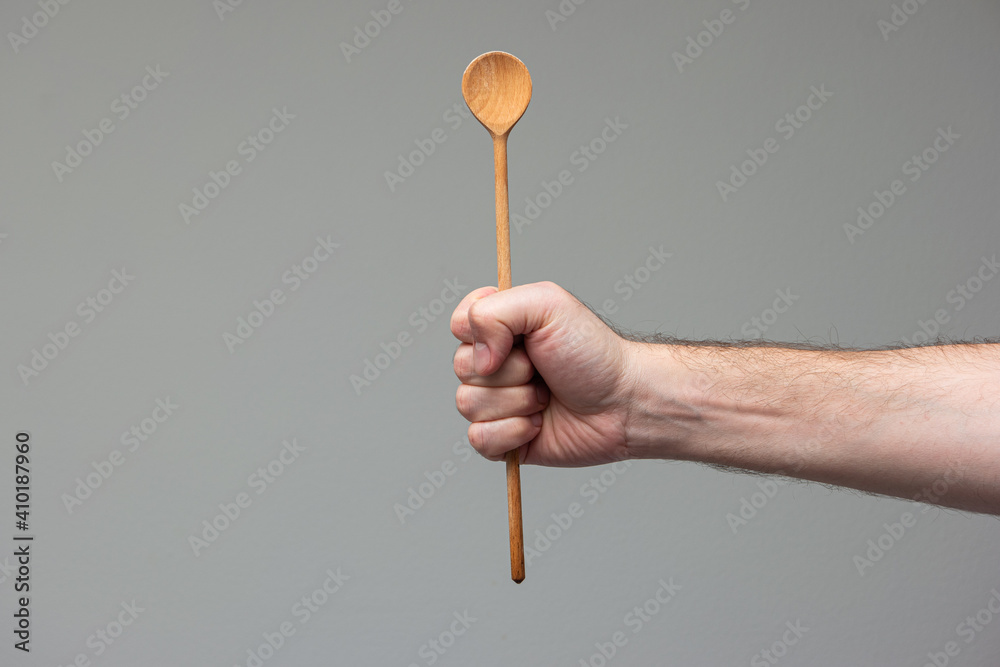 Caucasian male hand holding a wooden spoon close up shot isolated on gray background