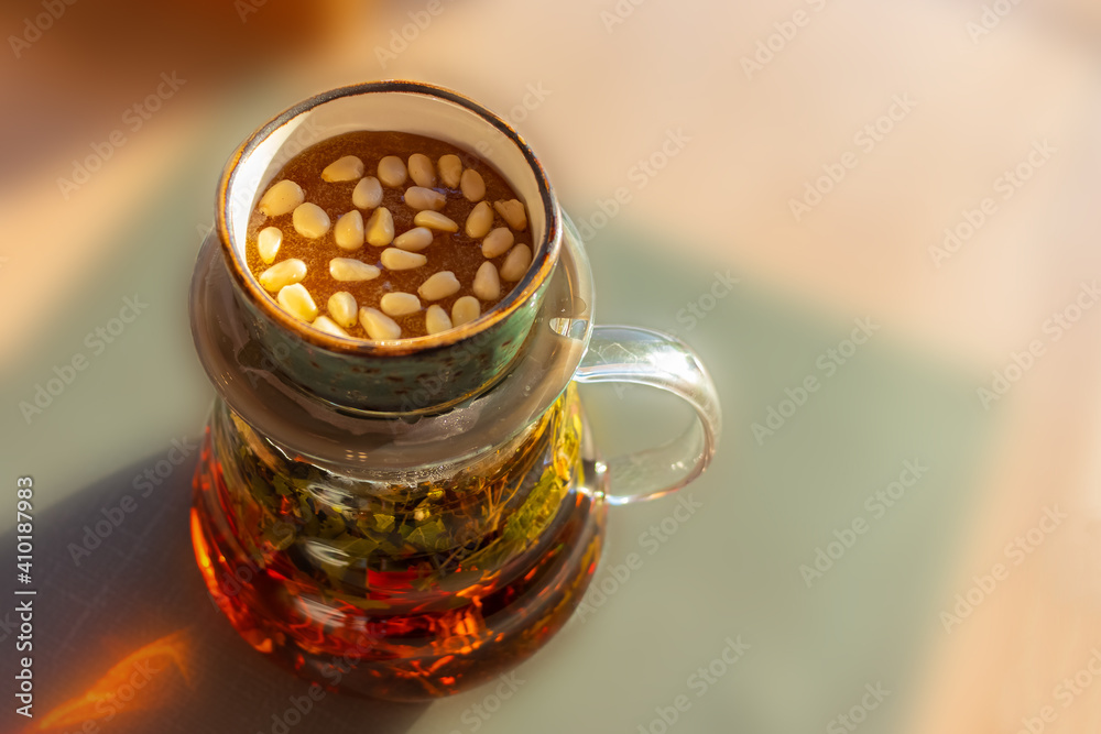 A saucer with honey and pine nuts is on the teapot A teapot with herbs is on the table on a sunny day. The background is blurred A saucer with honey and pine nuts is on the teapot A teapot with herbs is on the table on a sunny day. The background is blurred