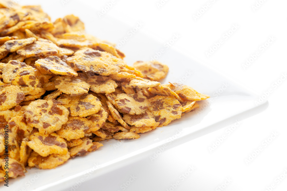 Spicy Chana Jor Garam in a white ceramic square plate, made with air-fried Bengal Chickpea. Pile of Indian spicy snacks (Namkeen), under backlight, side view, against the white background. Spicy Chana Jor Garam in a white ceramic square plate, made with air-fried Bengal Chickpea. Pile of Indian spicy snacks (Namkeen), under backlight, side view, against the white background.