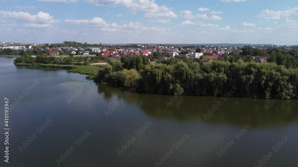 View of the river, houses and green trees on the shore. Outskirts of the city of Rivne. Summer. Drone Video. Ukraine. Europe
