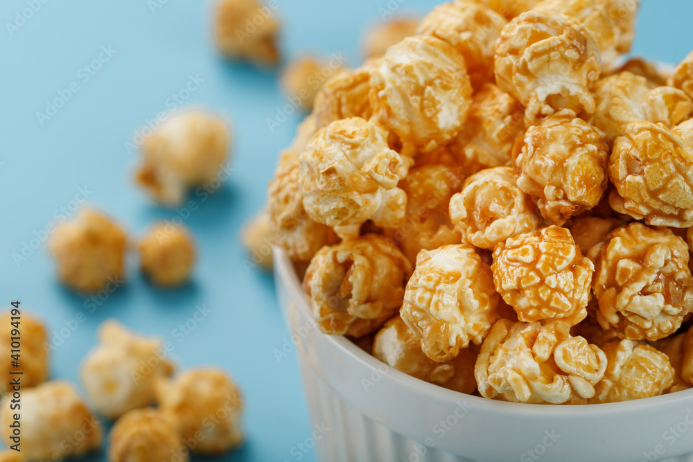 Caramel popcorn in a white glass cup with scissors on a blue background Caramel popcorn in a white glass cup with scissors on a blue background