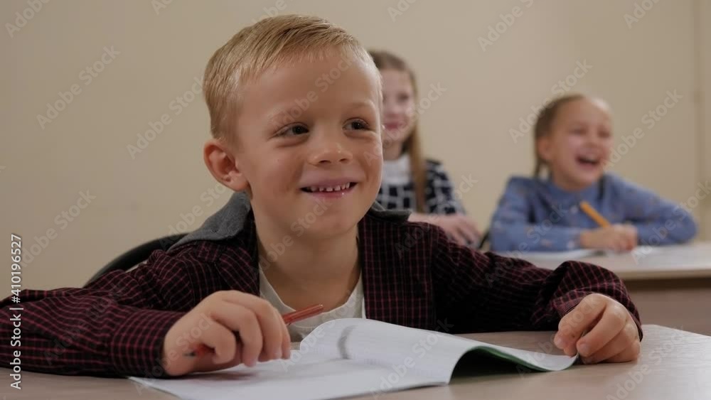 Close-up of a little boy sitting at a desk at school and laughing, interesting and fun lessons. Close-up of a little boy sitting at a desk at school and laughing, interesting and fun lessons.