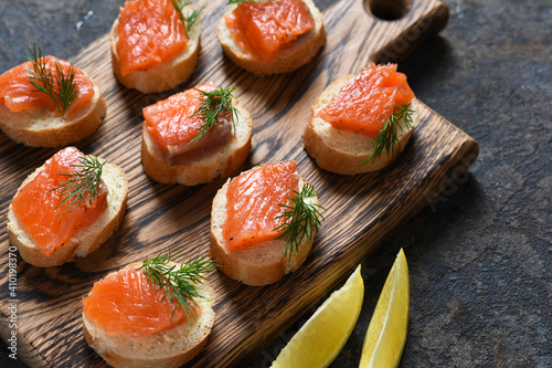 Toast from bread with butter and salmon on a wooden board on a concrete background. Breakfast. Fish canapes on the table.