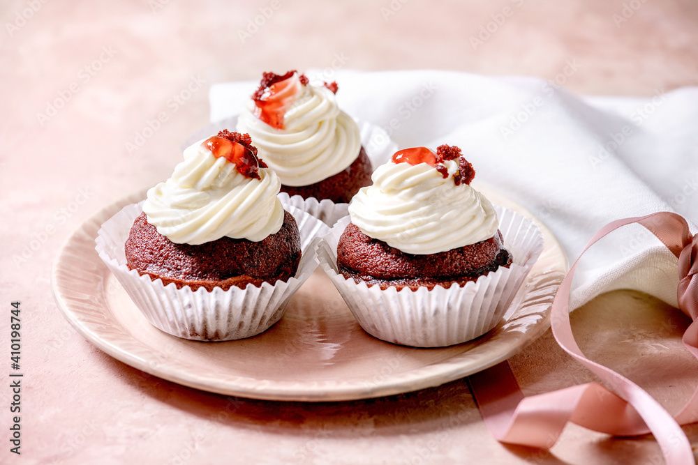 Homemade Red velvet cupcakes with whipped cream on pink ceramic plate, white napkin with ribbon over pink texture background. Homemade Red velvet cupcakes with whipped cream on pink ceramic plate, white napkin with ribbon over pink texture background.