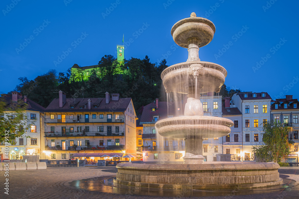 A water fountain at dusk in the heart of Slovenia's capital city Ljubljana, with the Ljubljana Castle in the perched on a hilltop in the background.