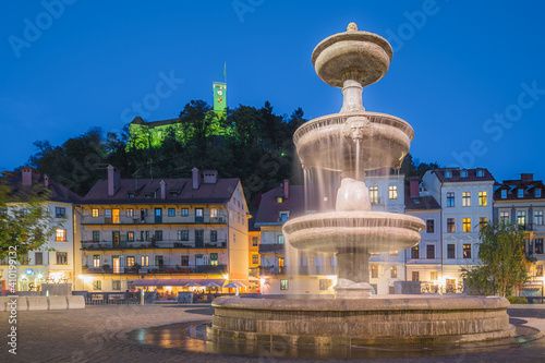 A water fountain at dusk in the heart of Slovenia s capital city Ljubljana  with the Ljubljana Castle in the perched on a hilltop in the background.