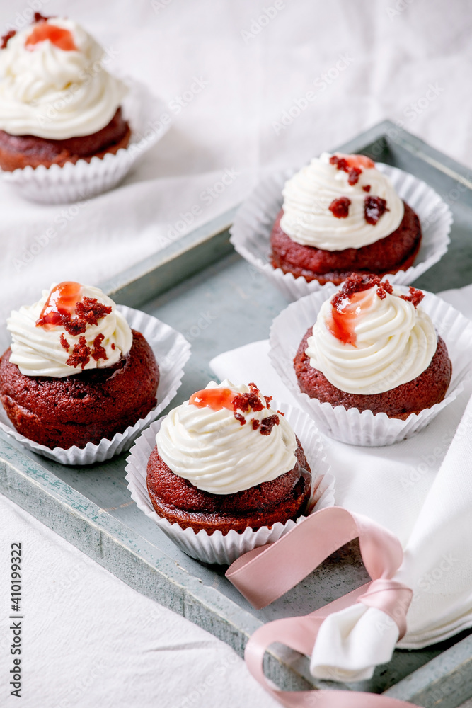 Homemade Red velvet cupcakes with whipped cream on wooden tray, white napkin with ribbon on white linen table cloth.