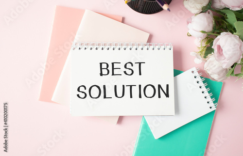 On a light pink background, there are notebooks and pencils and a notebook with the words BEST SOLUTION. Business concept