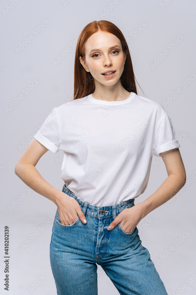 Joyful young woman wearing T-shirt and denim pants showing tongue on isolated white background. Pretty lady model with red hair emotionally showing facial expressions in studio, copyspace. Joyful young woman wearing T-shirt and denim pants showing tongue on isolated white background. Pretty lady model with red hair emotionally showing facial expressions in studio, copyspace.