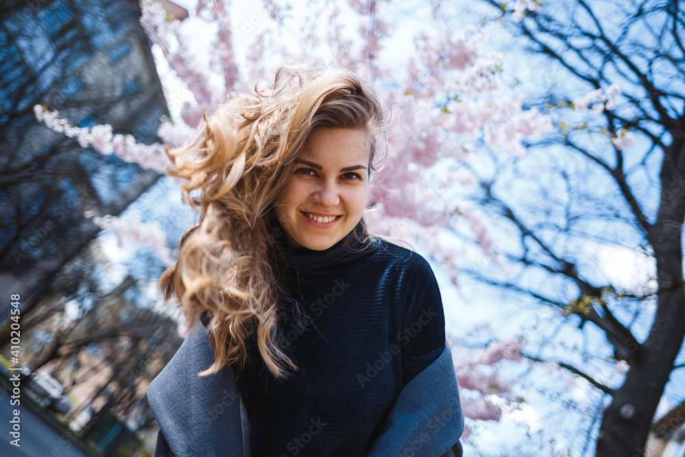 Sakura branches with flowers on a tree on the city streets. Happy woman girl spinning on the street with blooming sakura. Gorgeous fashionable girl outdoors. Sakura tree blossoms. Sakura branches with flowers on a tree on the city streets. Happy woman girl spinning on the street with blooming sakura. Gorgeous fashionable girl outdoors. Sakura tree blossoms.