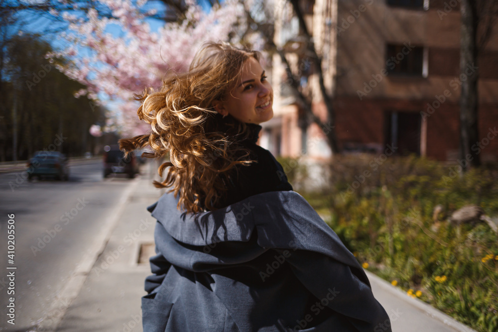Sakura branches with flowers on a tree on the city streets. Stylish woman girl runs on the street with blooming sakura. Gorgeous fashionable girl outdoors. Sakura tree blossoms. Sakura branches with flowers on a tree on the city streets. Stylish woman girl runs on the street with blooming sakura. Gorgeous fashionable girl outdoors. Sakura tree blossoms.