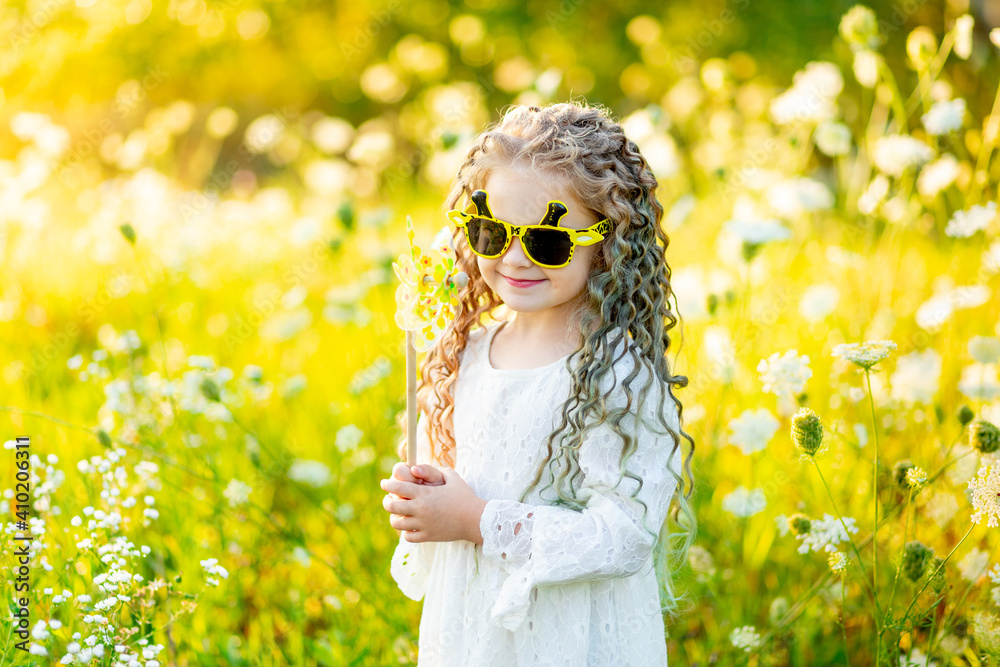 beautiful little girl in sunglasses in summer in a yellow field with flowers blowing on a turntable beautiful little girl in sunglasses in summer in a yellow field with flowers blowing on a turntable