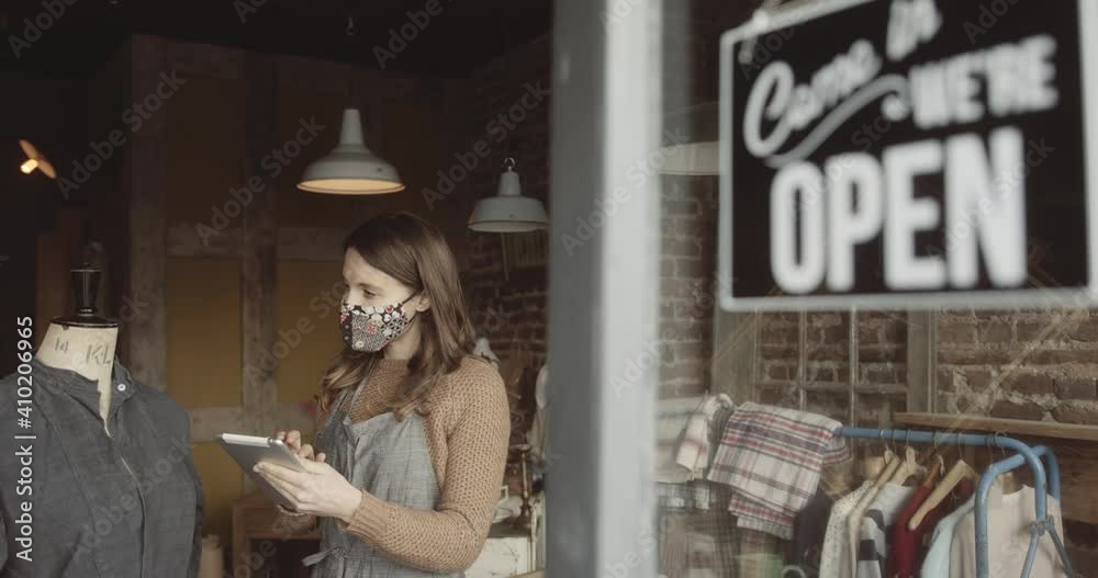 Young adult Female working in store using digital tablet taking inventory with open sign on door Young adult Female working in store using digital tablet taking inventory with open sign on door
