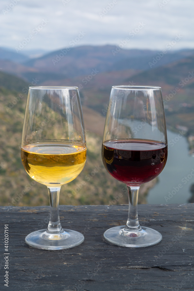 Glasses of Portuguese fortified port wine, produced in Douro Valley and Douro river with colorful terraced vineyards on background in autumn, Portugal