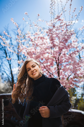 Sakura branches with flowers on a tree on the city streets. Stylish woman girl stands in the street with blooming sakura. Modern fashionable girl outdoors. Sakura tree blossoms. © Дмитрий Ткачук